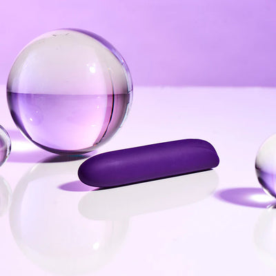 Purple silicone bullet vibrator displayed with clear glass spheres on a reflective surface with a soft purple background.