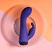 Purple silicone dual stimulator vibrator with curved design on a textured clear plate against a peach and pink background.