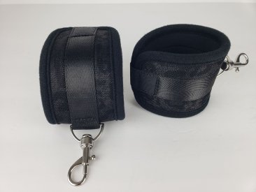 Black neoprene wrist restraints with adjustable Velcro straps and metal lobster clasps for secure attachment.