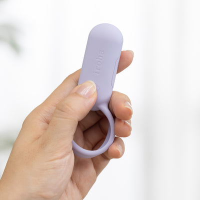 Hand holding a compact lavender Iroha Svr Ring vibration device with a silicone loop handle against a soft white background.