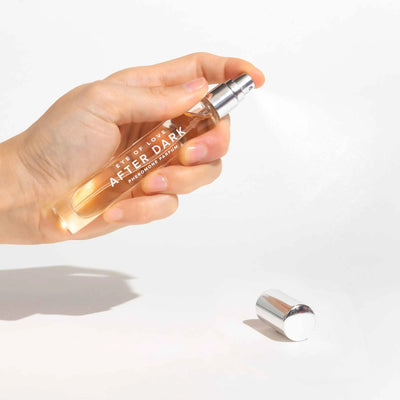 Hand holding Eye of Love After Dark pheromone perfume spray with silver cap on white background.