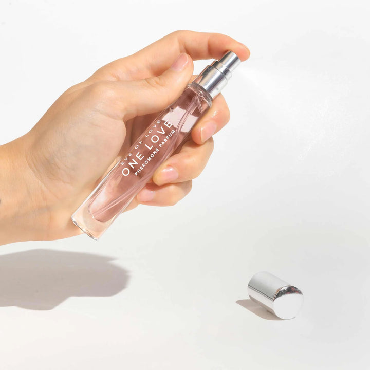 Hand holding Eye of Love One Love pheromone perfume spray bottle with silver cap on white background
