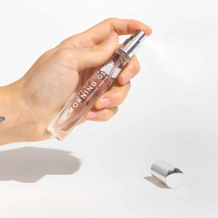 Hand holding Eye of Love Morning Glow pheromone perfume spray with silver cap on white background