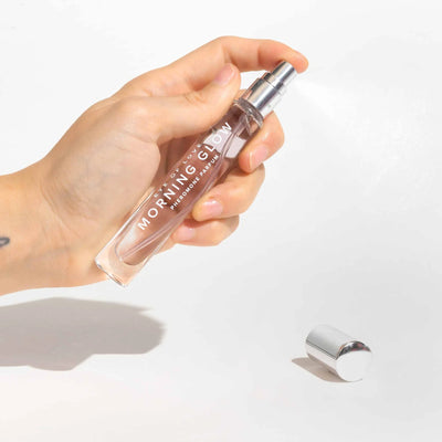 Hand holding Eye of Love Morning Glow pheromone perfume spray with silver cap on white background