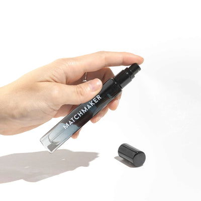 Hand holding Eye of Love Matchmaker Black Diamond pheromone perfume spray with cap off on white background