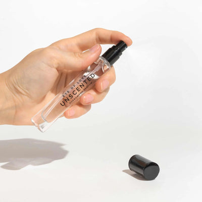 Hand holding Eye of Love Unscented Pheromone Parfum spray bottle with black cap on white background.