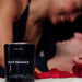 Eye of Love Matchmaker pheromone massage candle with red rose petals and a smiling couple in the background.