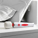 Adam & Eve Magic Massager Deluxe white and red electric wand massager on a bedside table with pillow in background