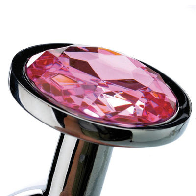 Close-up of a medium-sized polished metal anal plug featuring a large faceted pink gem at the base.