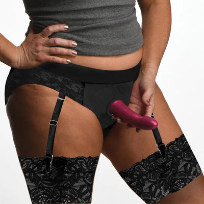 Black panty harness with lace garter straps worn with matching thigh-high stockings, featuring a front O-ring for strap-on attachment.