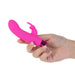 Hand holding a compact pink silicone vibrator with a removable rabbit-shaped sleeve and metallic base.
