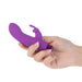 Hand holding a compact purple silicone vibrator with a removable rabbit-shaped sleeve and metallic base.