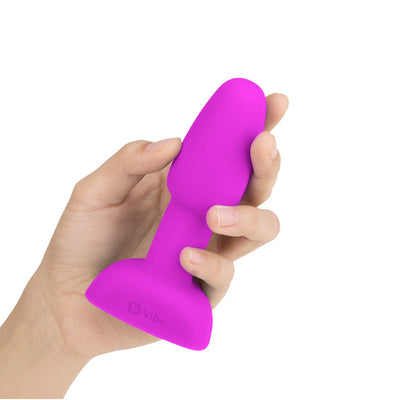 Hand holding a compact, bright purple silicone vibrating rimming plug with a flared base.