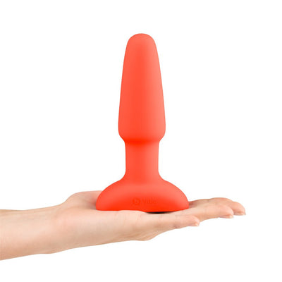 Hand holding a bright red silicone B-Vibe Rimming Plug 2 with a tapered tip and wide base on a white background.