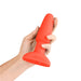 Hand holding a bright red silicone B-Vibe Rimming Plug 2 with a flared base on a white background.