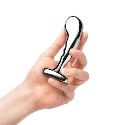 Hand holding a polished stainless steel prostate training plug with a curved, tapered design and flared base.