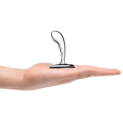 Hand holding a polished stainless steel prostate plug with a curved, textured design and wide base.