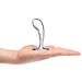 Hand holding a polished stainless steel prostate plug with a curved, textured design and wide base.