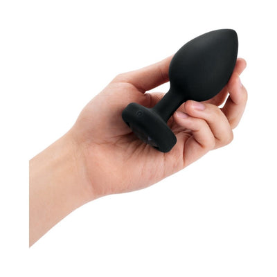 Hand holding a black silicone vibrating jewel plug with a rounded tip and jeweled base.