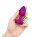 Hand holding a small purple silicone vibrating plug with a tapered tip and flat base with power button.