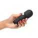 Hand holding a compact black silicone mini wand vibrator with textured head and control buttons.