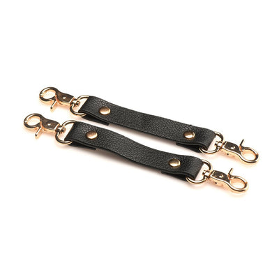 Two black vegan leather cuff connectors with gold metal clasps and rivets on a white background.