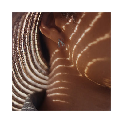 Close-up of an ear wearing a delicate sterling silver Biird Clit Earring with artistic light patterns on the skin.