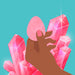 Hand holding a smooth rose quartz egg with pink crystals in the background on a teal backdrop.