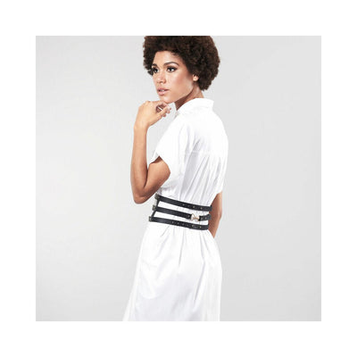 Woman wearing a white dress styled with Bijoux Indiscrets Maze wide black vegan leather belt restraints at the waist.