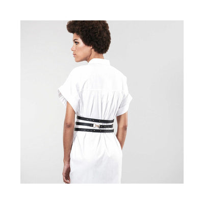 Woman wearing a white dress styled with Bijoux Indiscrets Maze wide black vegan leather belt restraints at the waist.