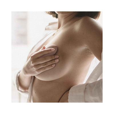 Woman using a compact, curved pink vibrating massager on her breast, wearing a white robe.