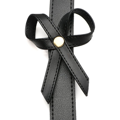 Close-up of black faux leather thigh harness strap with decorative bow and gold-tone rivet detail.