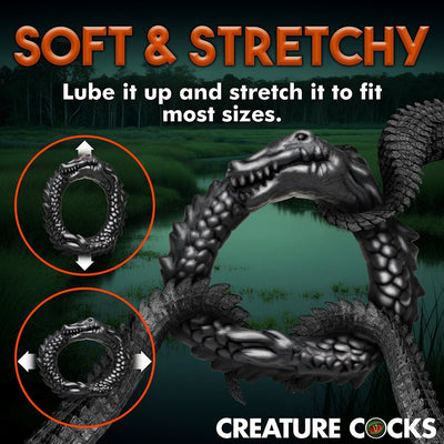 Black silicone caiman-shaped cock ring shown stretched vertically and horizontally to highlight its soft, stretchy material.