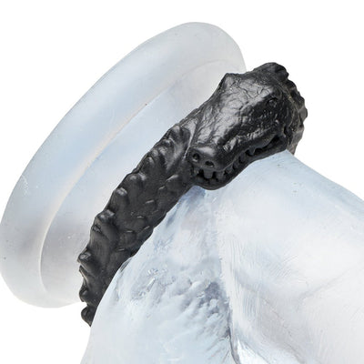Black silicone cock ring featuring a textured caiman design with ridges and a grinning face.