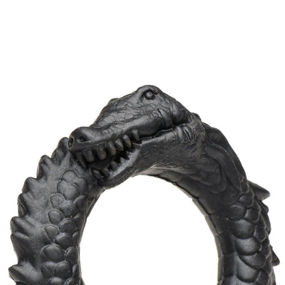 Close-up of a black silicone cock ring shaped like a smiling caiman with textured ridges and detailed scales.