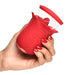 Hand holding a red silicone flower-shaped personal massager with control buttons and a clear suction cup top.