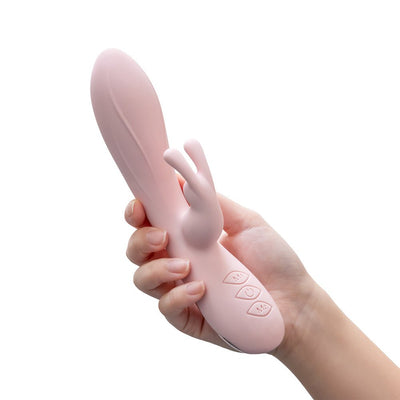 Hand holding a blush pink dual-stimulation rabbit vibrator with ergonomic buttons and smooth silicone finish.