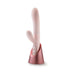 Blush pink dual-stimulation vibrator with curved shaft and clitoral arm in a rose gold charging stand.