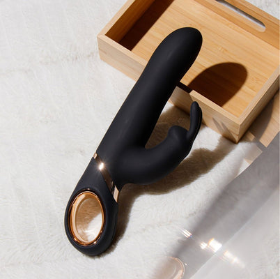 Black silicone rabbit vibrator with gold accent and ergonomic handle resting on white fabric near wooden box.