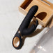 Black silicone rabbit vibrator with gold accent and ergonomic handle resting on white fabric near wooden box.