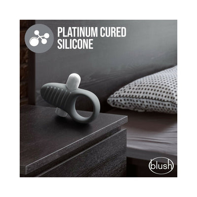 Slate gray silicone ring with textured ridges and a removable bullet vibrator displayed on a dark bedside table.