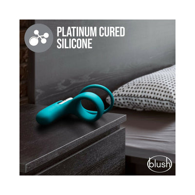 Teal silicone Blush Noje C2 Ring resting on a dark bedside table with a bed and pillow in the background.