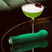 Green satin-smooth G-spot vibrator with faceted gem base next to a green cocktail on a reflective surface.