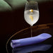 Sleek purple vibrator with faceted gem-like base resting on a reflective surface beside a glass of water with lemon peel.