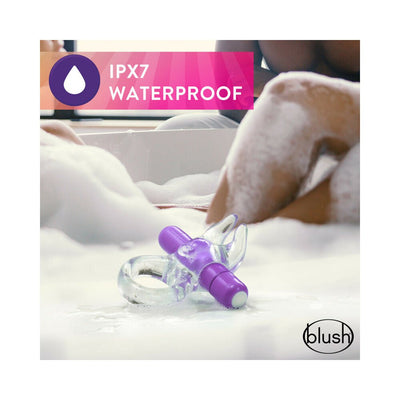 Clear vibrating C-ring with purple bullet and soft ears placed in a bubbly bath, highlighting its waterproof feature.