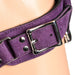 Close-up of purple suede leather corset harness strap with silver metal buckle and rivets on skin tone background.