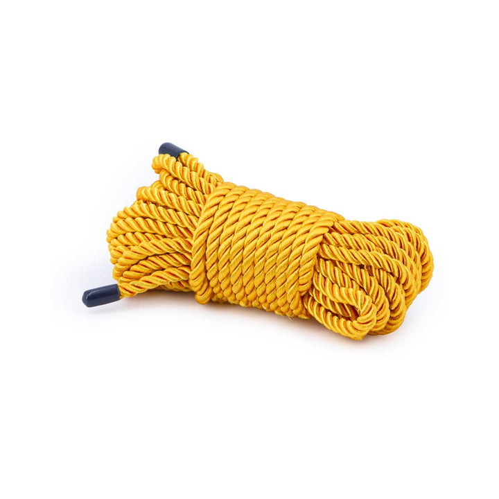 Coiled gold synthetic bondage rope with black capped ends on white background.