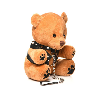 Light peach plush teddy bear wearing black faux leather harness with metal chain leash and paw prints on feet and hands.