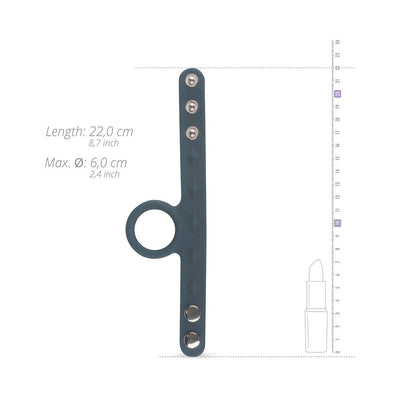 Black silicone cock and ball strap with adjustable snap closures shown next to measurement scale and lipstick for size reference.