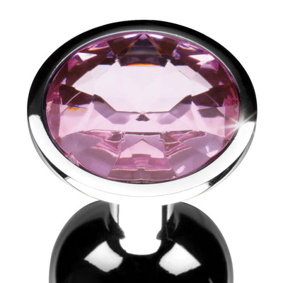 Close-up of a small metal anal plug with a smooth black finish and a large pink gem at the base.